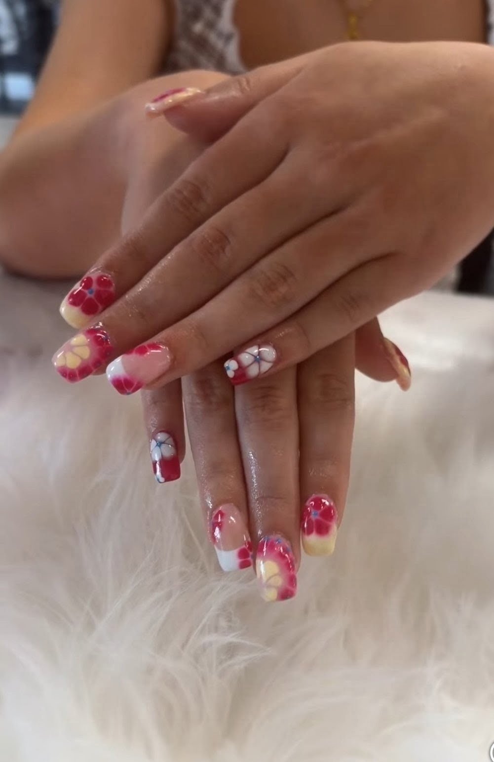 Short square nails with hand-painted red, yellow, and white flowers on a fluffy white rug