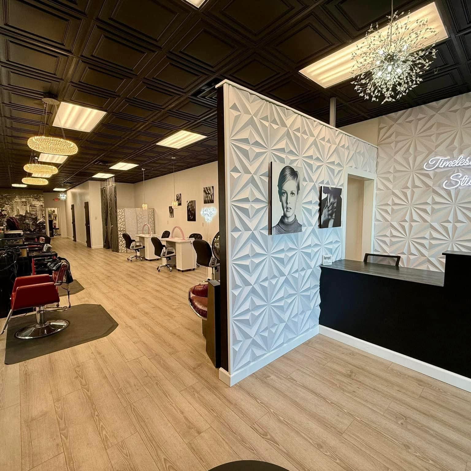 The front of Timeless Hair Studio with a geometric white feature wall, black-and-white portraits, crystal chandelier, and the studio's neon sign