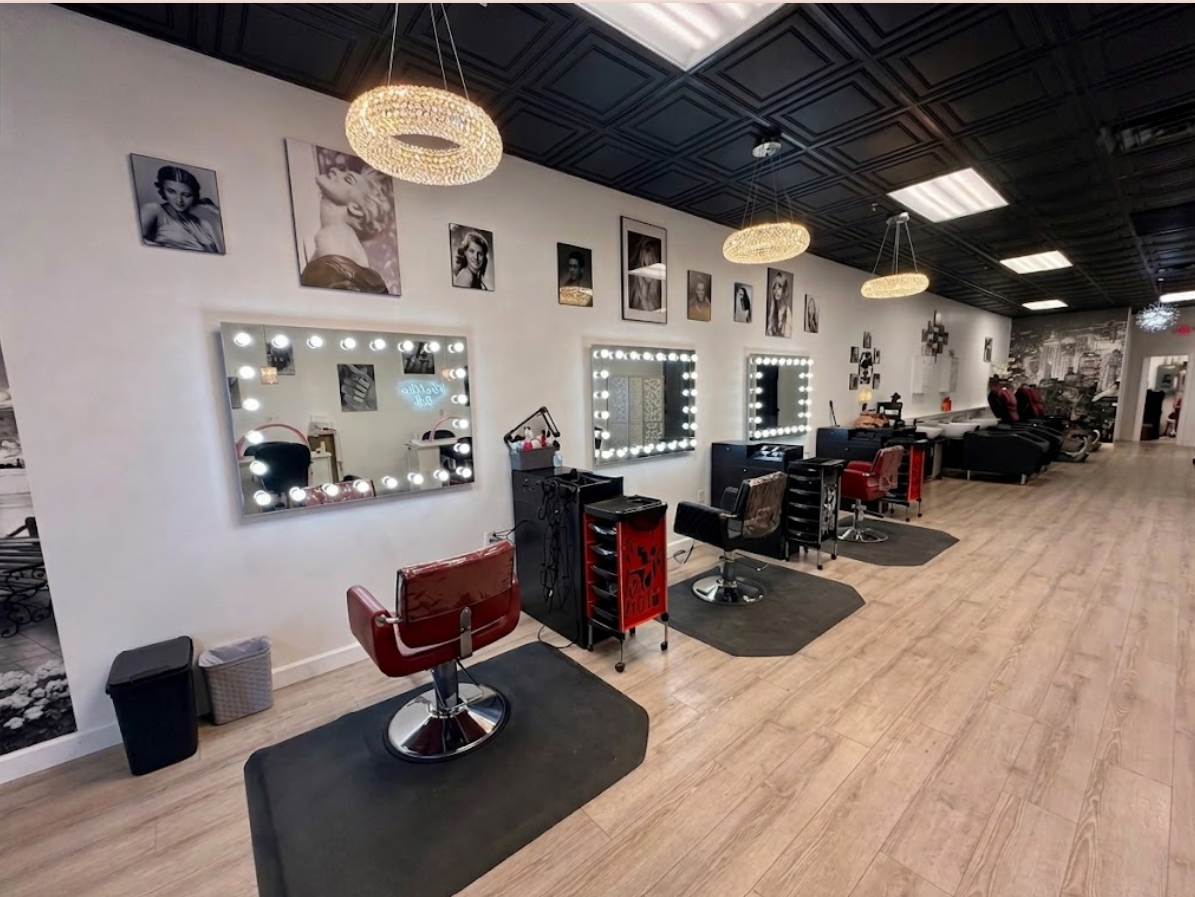 Styling stations at Timeless Hair Studio with lit vanity mirrors, red salon chairs, and vintage black-and-white portraits