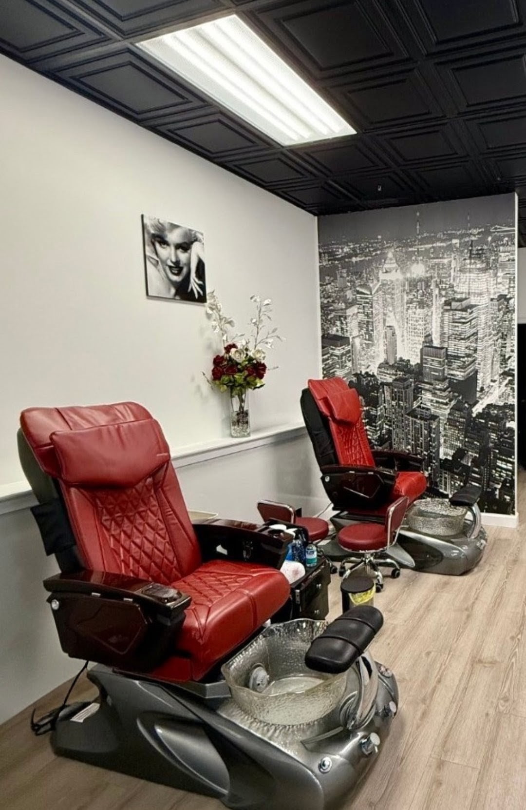Two red leather pedicure chairs in front of a black-and-white New York skyline mural
